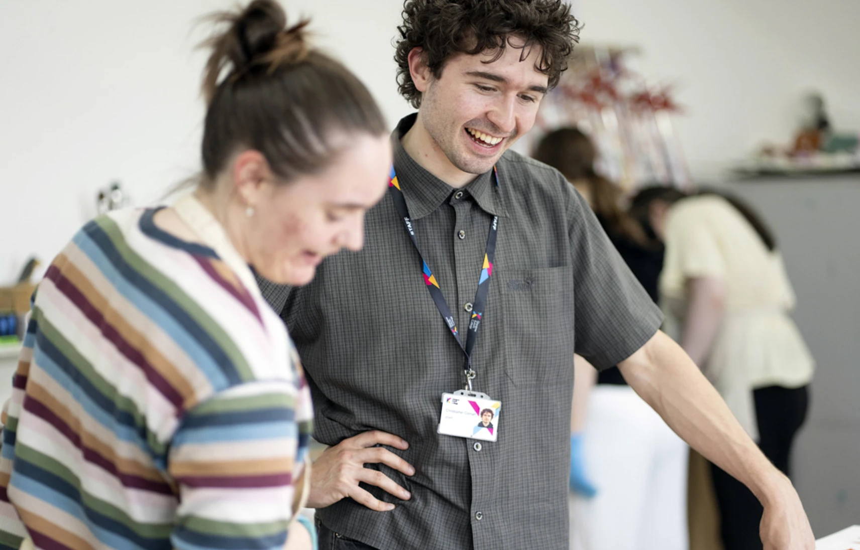 Two people discussing artwork in a studio, with others working in the background. Two people discussing artwork in a studio, with others working in the background.